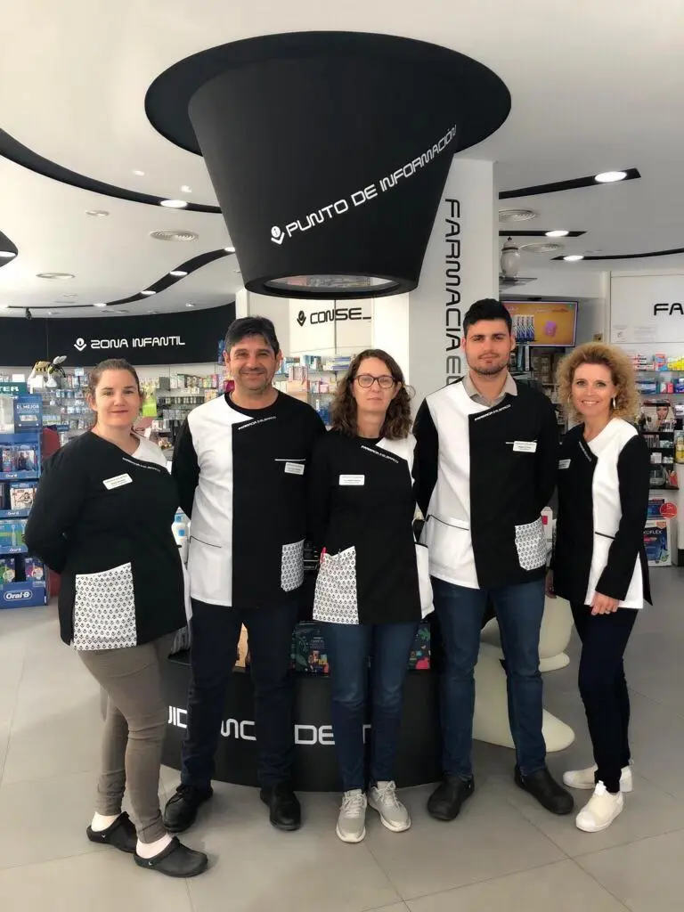 Equipo de la farmacia con uniforme blanco y negro posando junto al punto de información