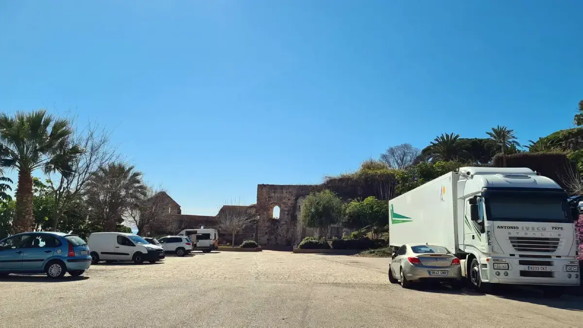 Explanada de tierra del parking con furgonetas, un camión y los restos de un muro antiguo