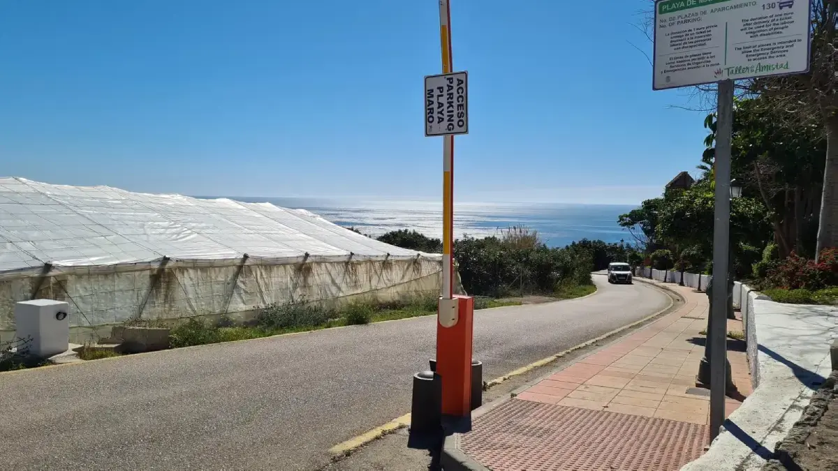 Barrera de entrada con el cartel de acceso al parking de la playa de Maro y el mar al fondo