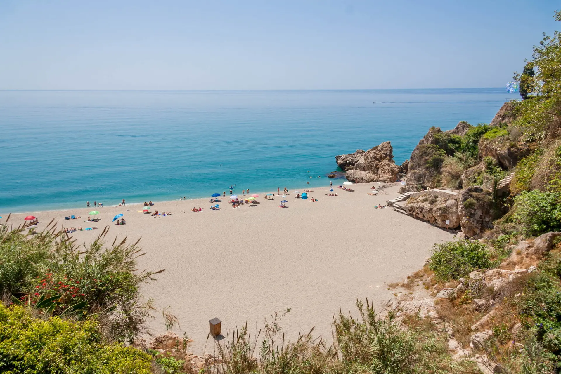 Cala Carabeillo con sombrillas en la arena y la escalera de bajada entre las rocas