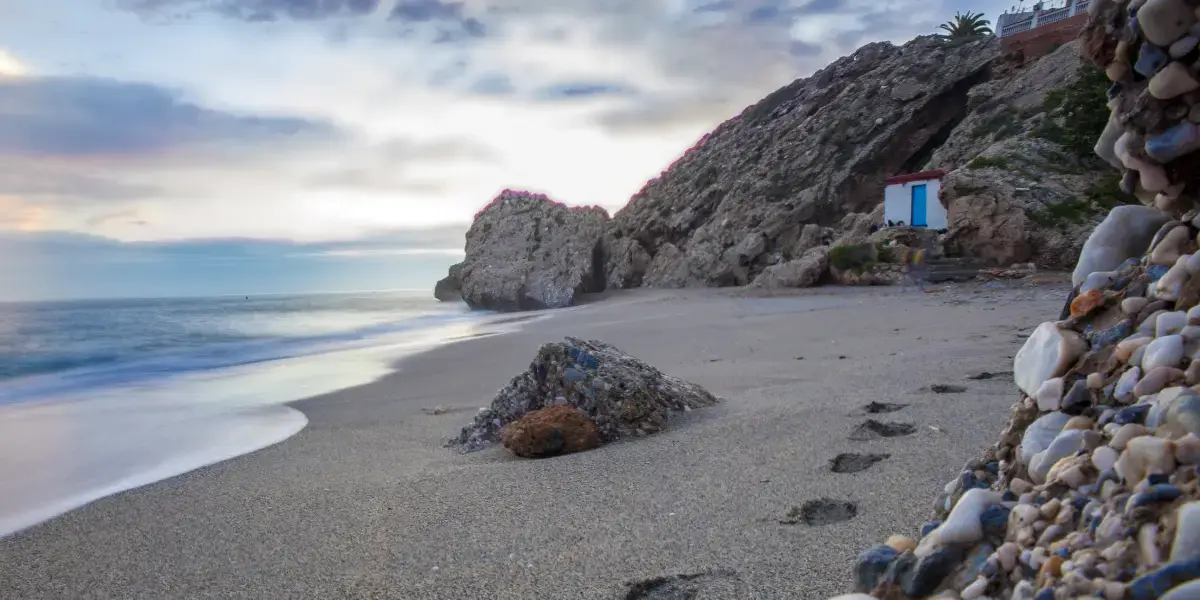 Arena de la playa Carabeo al amanecer, con la casita blanca y azul entre las rocas