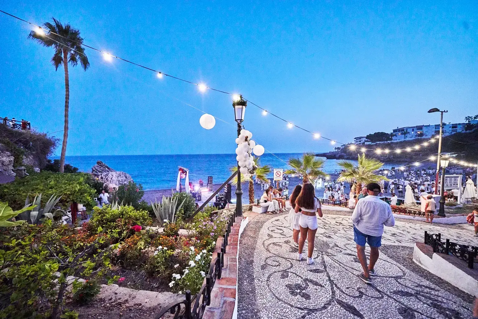 Bajada empedrada hacia la playa El Salón con guirnaldas de luces y el mar al anochecer
