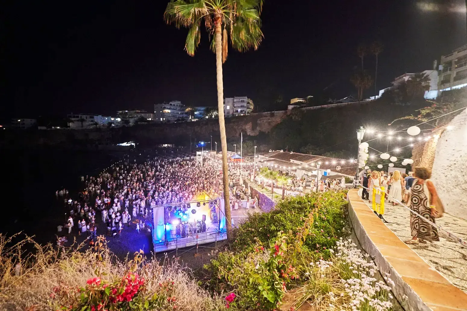 Vista nocturna desde lo alto de la escalera, con la playa abarrotada y el escenario entre palmeras