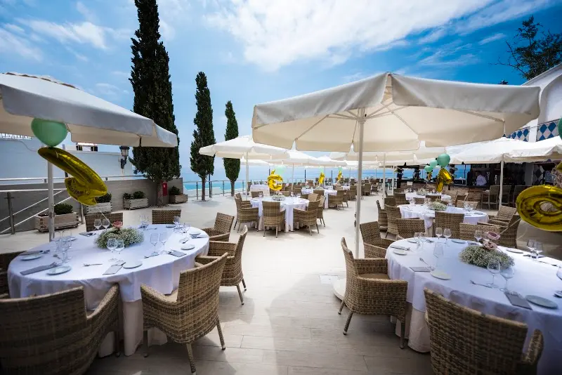 Tables with white cloths and gold balloons set for a celebration on the seafront terrace