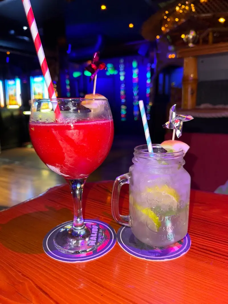 A frozen red cocktail in a balloon glass and a lime highball in a glass jar