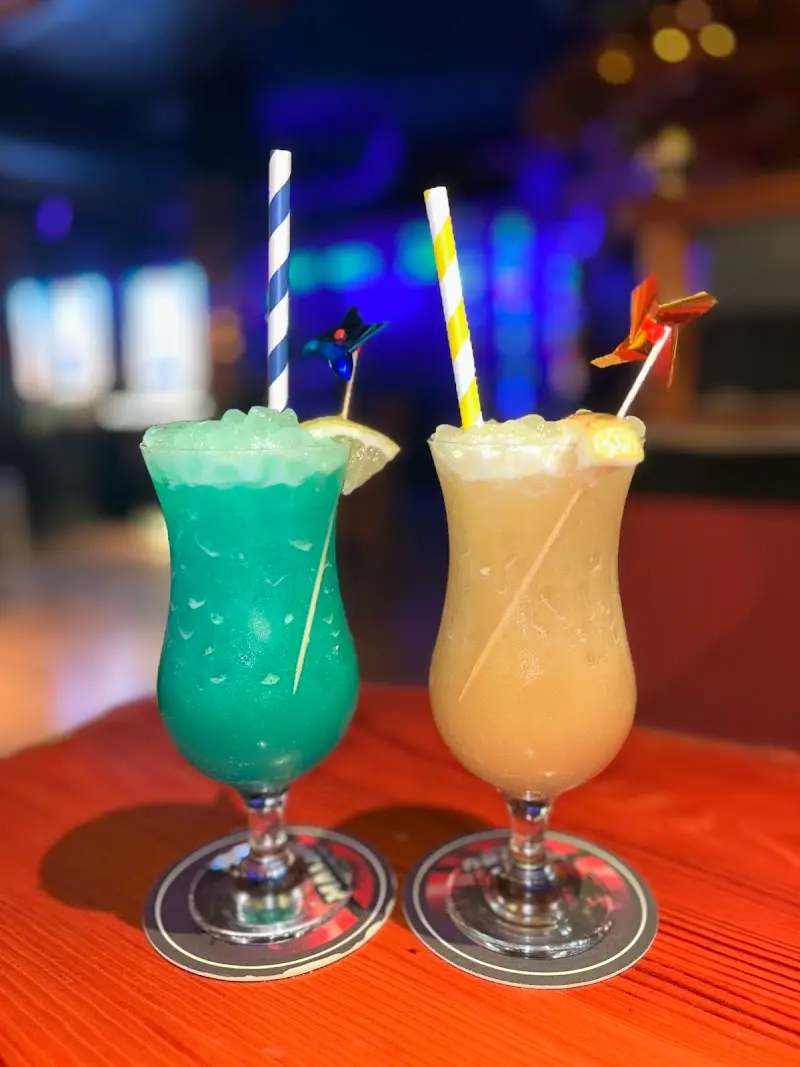 Two tropical cocktails, one blue and one creamy, with striped straws and paper windmills