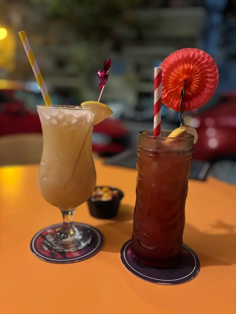 A creamy cocktail with lemon and a red one with a paper parasol on an orange table