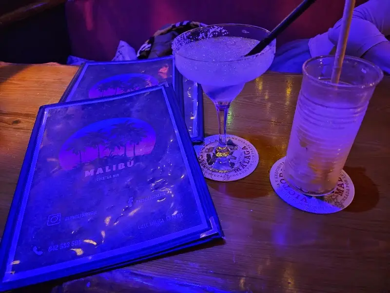 Malibu menus under blue light beside a margarita and a long drink