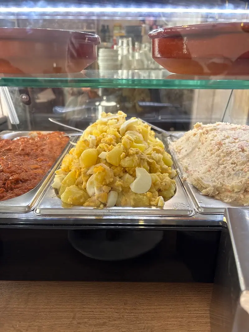 Potato salad with boiled egg among other trays of tapas in the display case