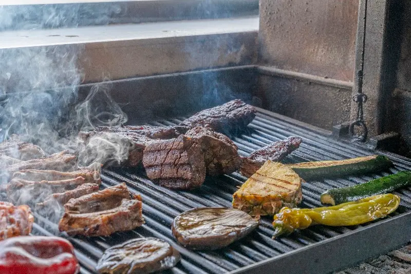 Meat and vegetables smoking on the Argentine grill: ribs, steak, courgette and peppers