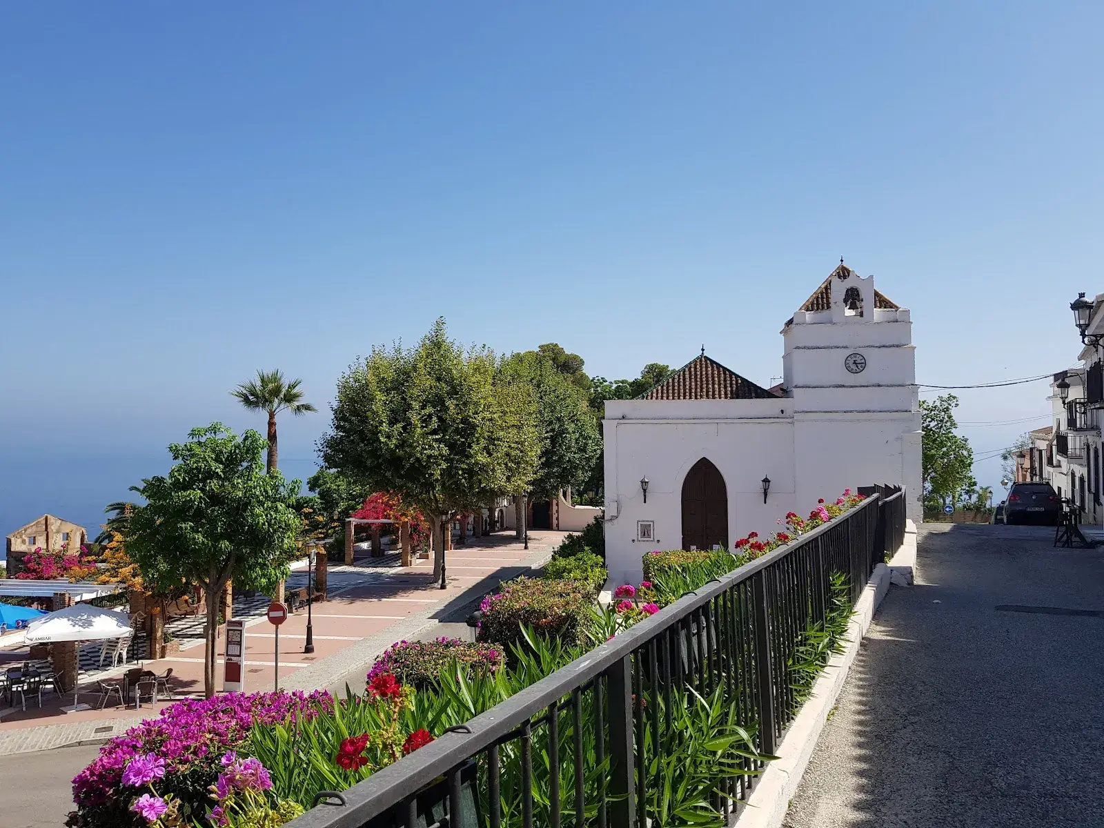 Iglesia blanca de Maro y la plaza con flores, terrazas y el mar al fondo