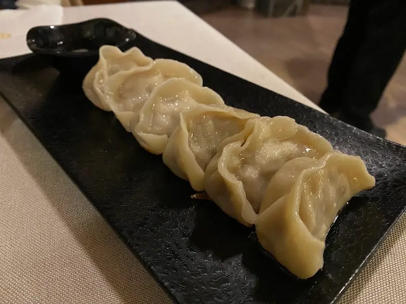 A row of steamed gyoza on a slate tray with a dipping bowl