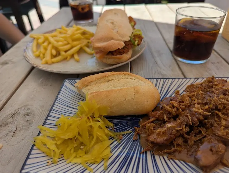 Pulled meat with bread and pickles, and a sandwich with chips on a wooden table