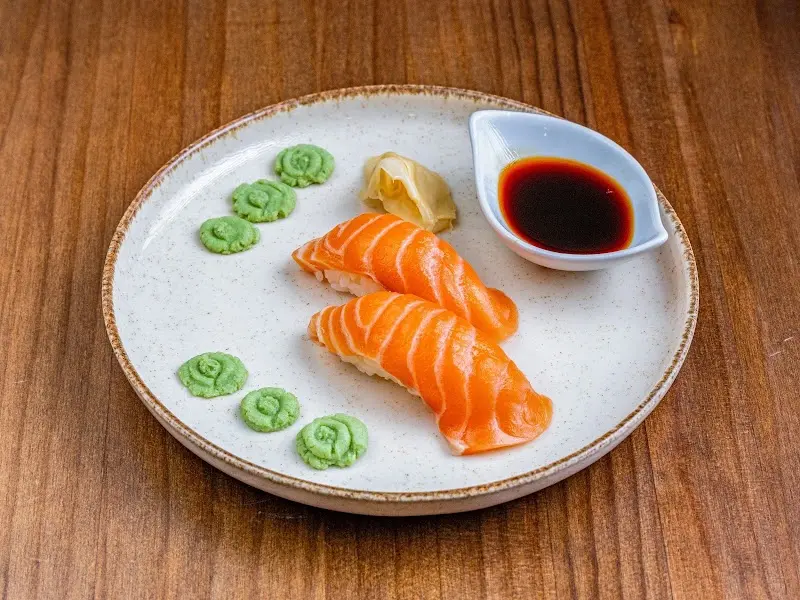 Two salmon nigiri with pickled ginger, wasabi and soy sauce on a pale plate