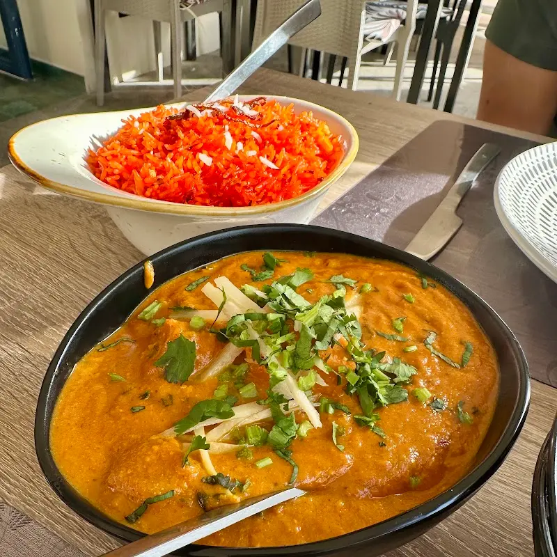 Curry in an orange sauce with ginger and coriander beside a bowl of coloured rice