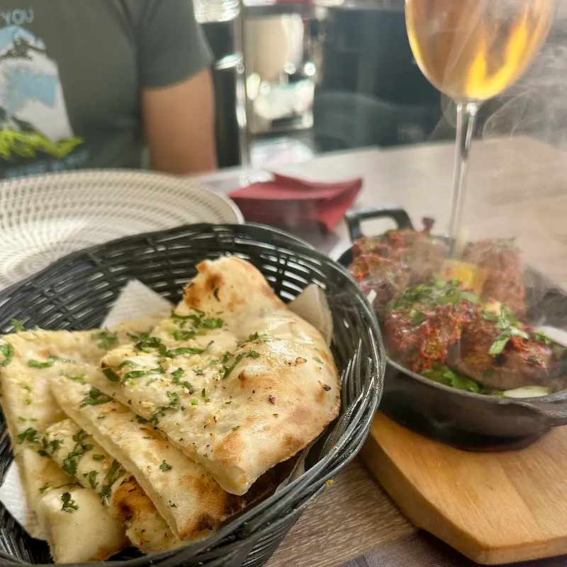 Basket of naan bread with herbs and sizzling meat in a cast-iron pan