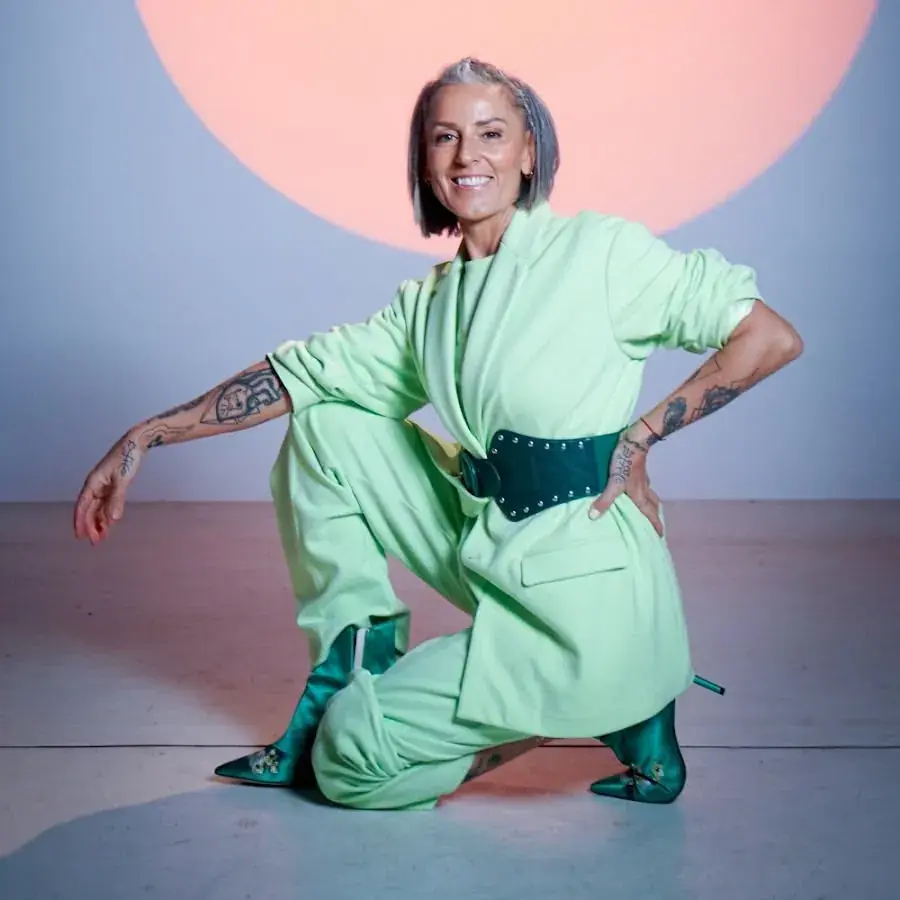 Artista invitada posando con traje verde claro ante un fondo con círculo rosado